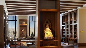 Un vestíbulo amplio con un expositor central de madera, una zona de estar con sofás y una gran estantería llena de libros y objetos decorativos.