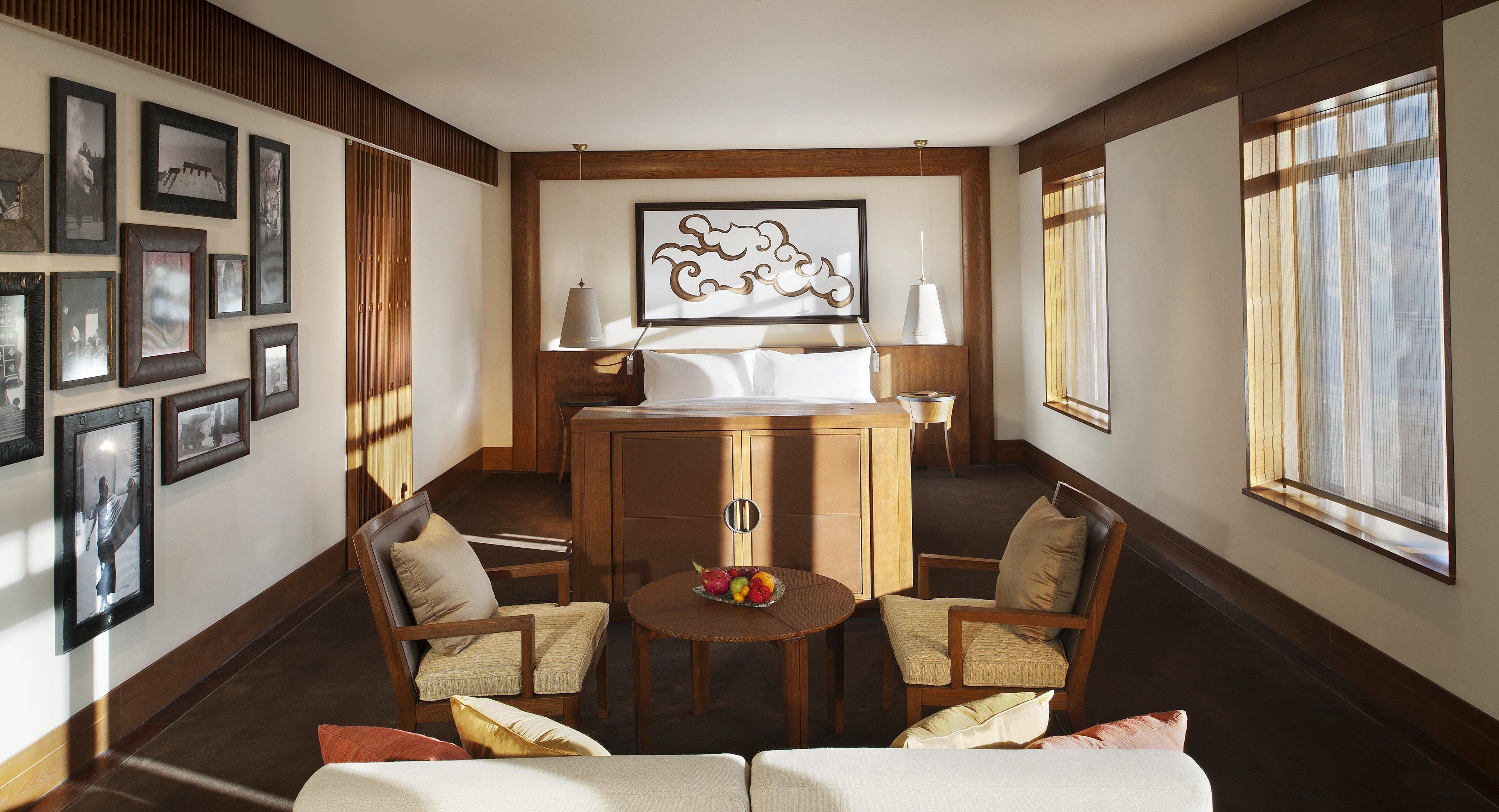 A hotel room with a bed, a desk, a chair, a small table with fruit, and framed pictures on the wall.