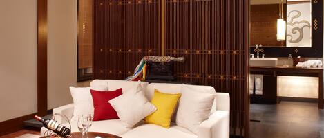A modern living room with a white sofa, a round wooden coffee table, and a decorative wall panel.
