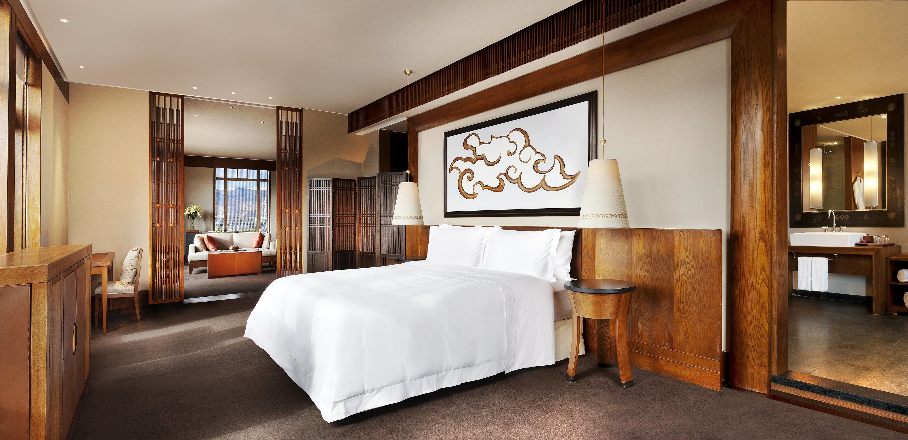 A hotel room with a large bed, a wooden headboard, a side table, a mirror, and a view of the city.