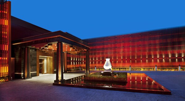 A modern building with a reflective water feature and a red-lit facade.