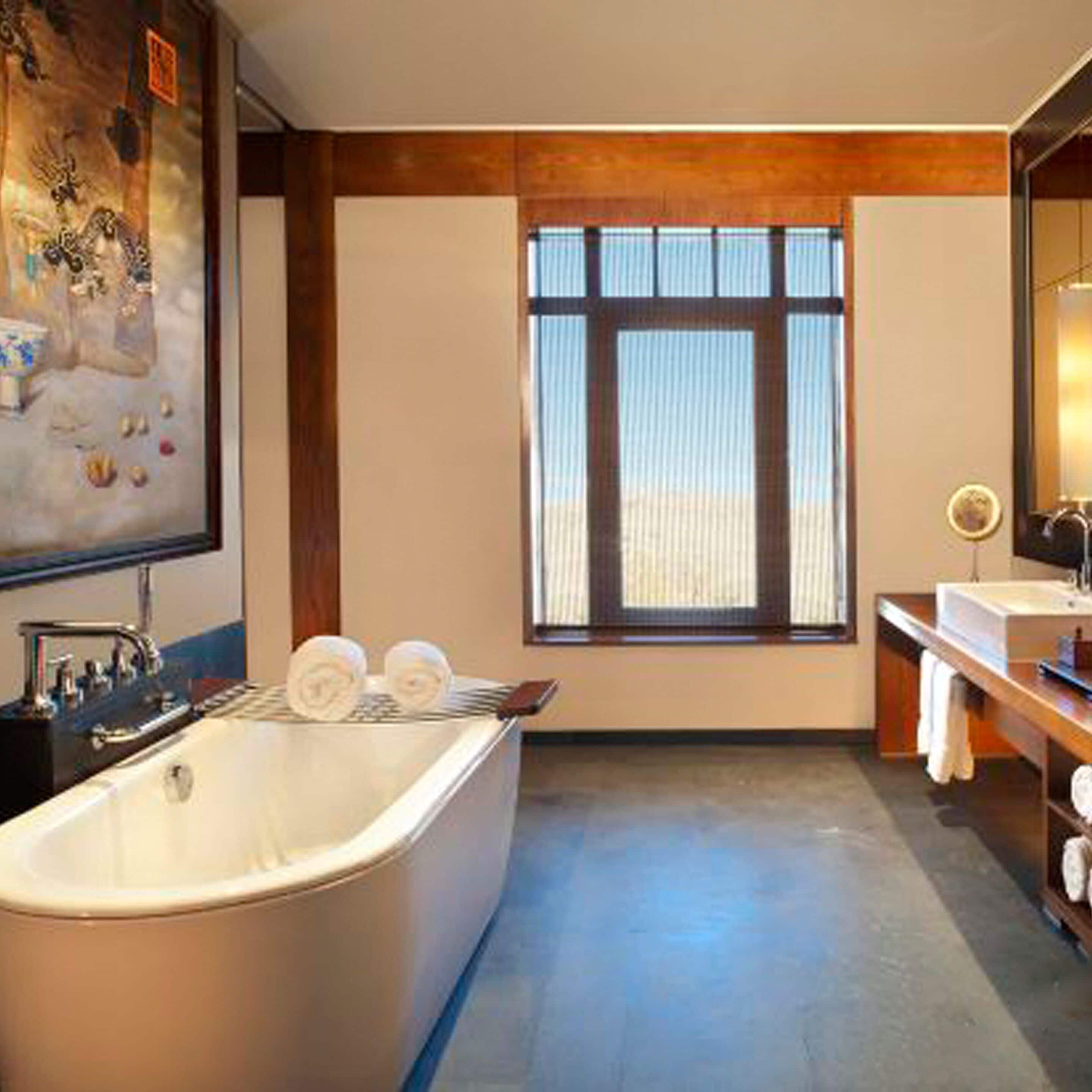 Een moderne badkamer met een vrijstaand bad, een groot raam en een schilderij aan de muur.