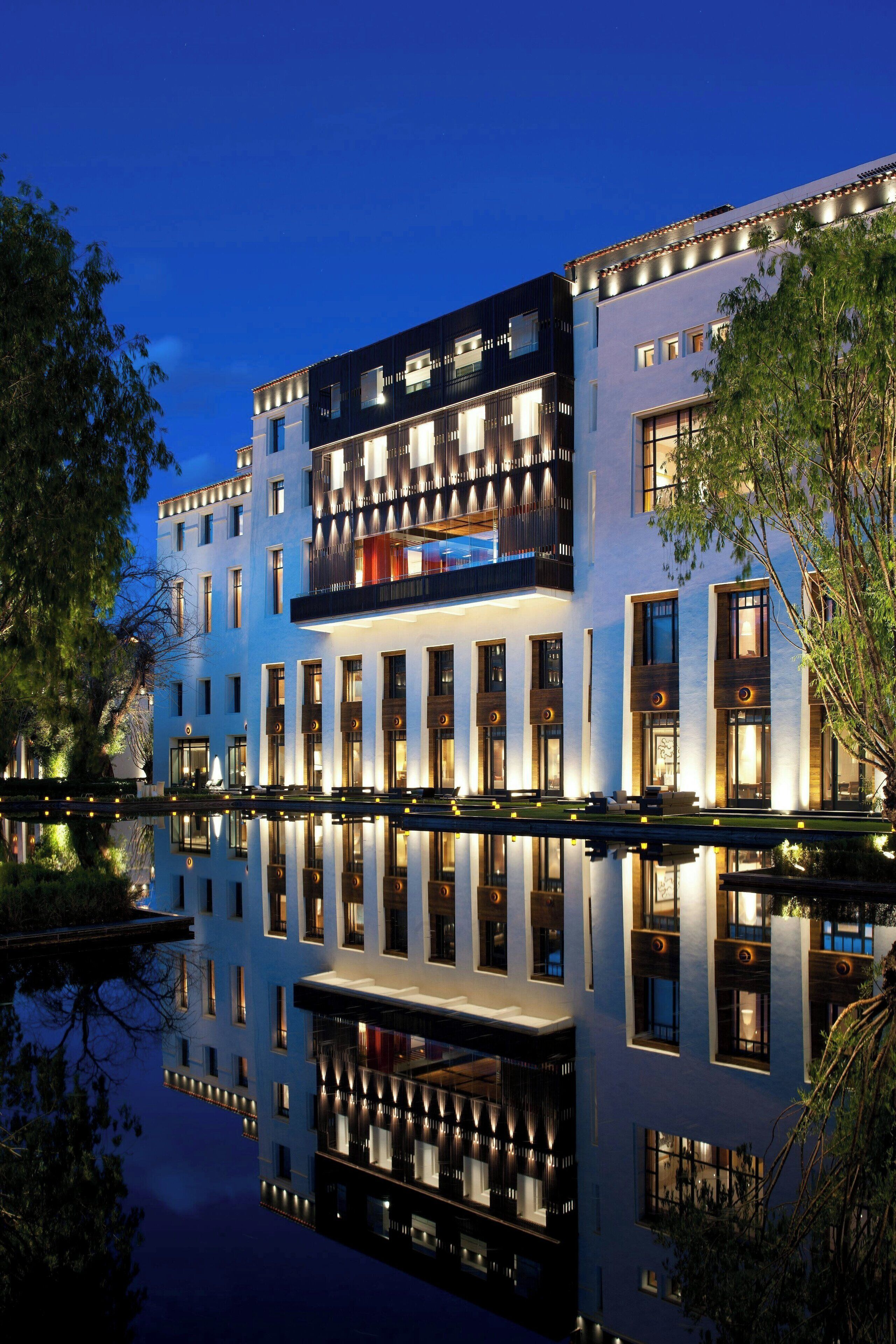 A modern hotel with a reflective pool in front, featuring a multi-story structure with balconies and large windows.