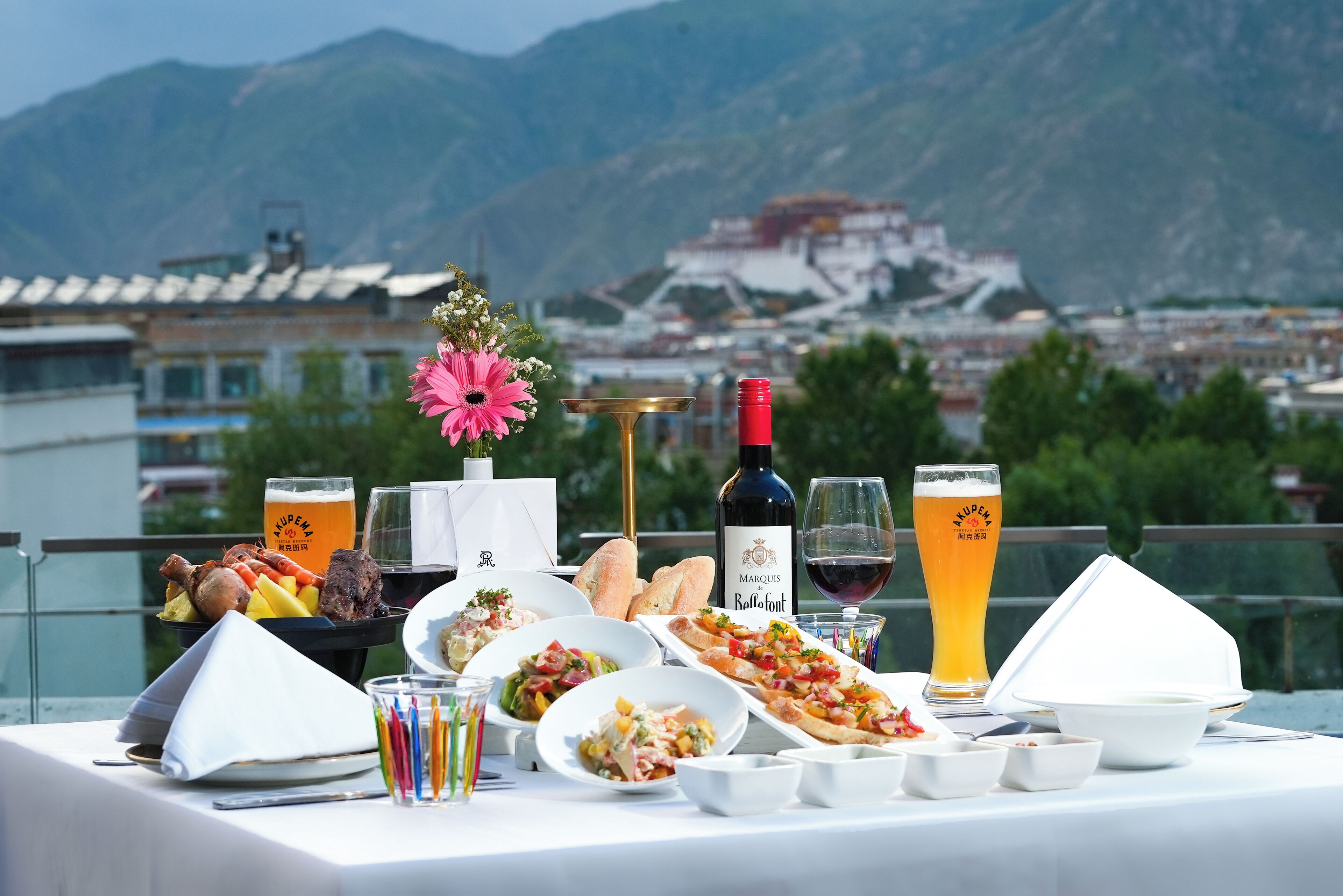 Une table dressée avec de la nourriture, des boissons et un bouquet de fleurs, donnant sur un paysage montagneux.