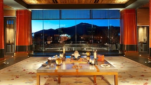 A room with a large window offering a mountain view, a wooden ceiling, and a table with various items.