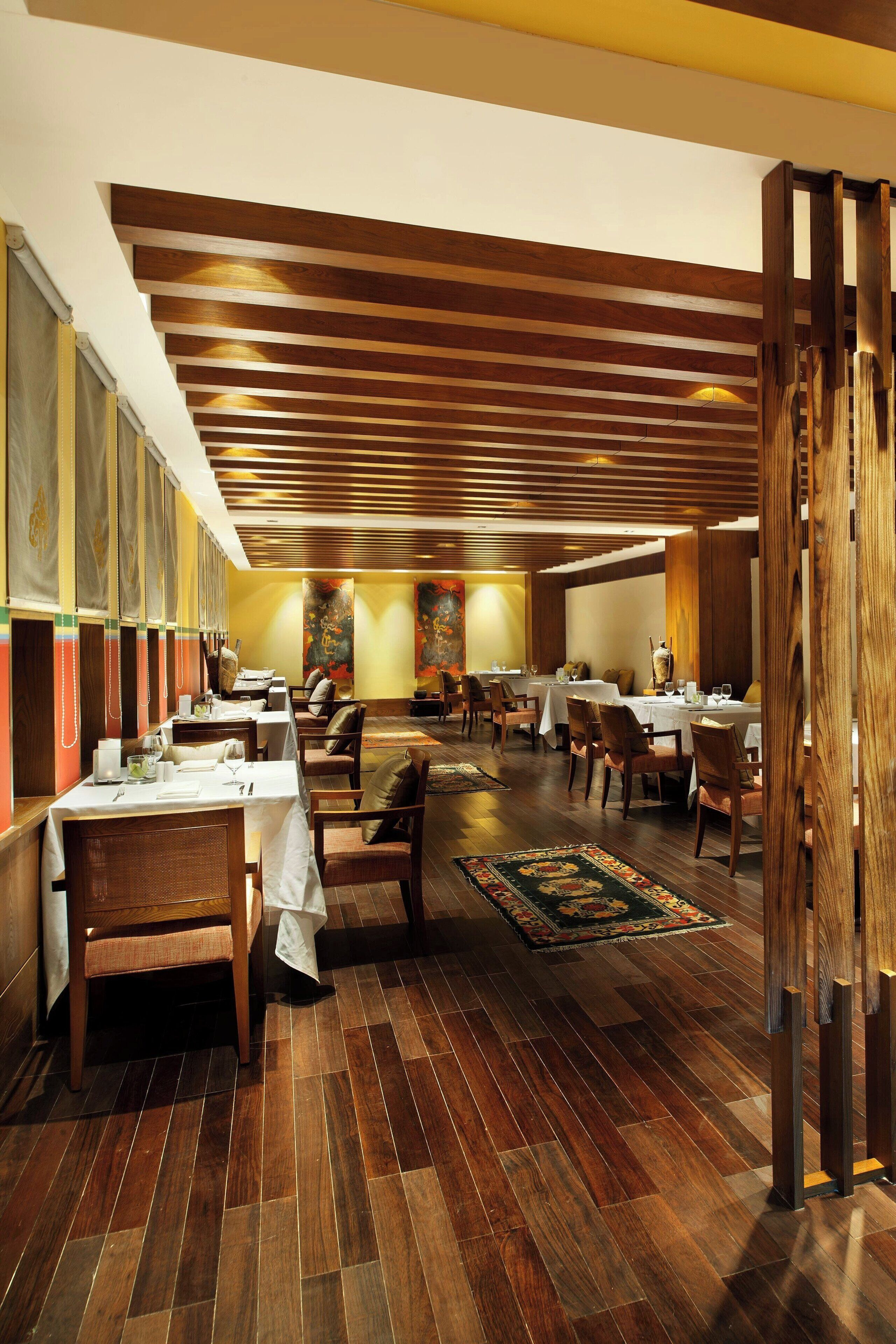 A restaurant with wooden flooring, tables, chairs, and a decorative ceiling.