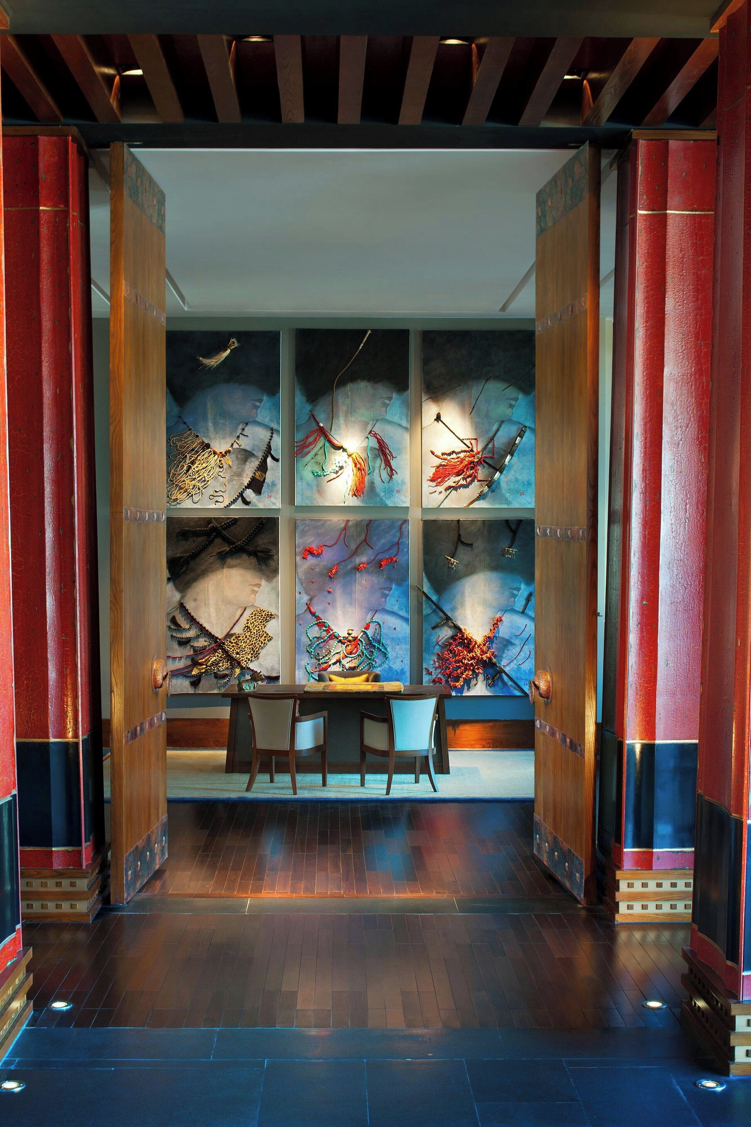 A room with a wooden floor, a desk, and chairs. There are large windows with artwork on the walls.