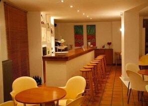 Ein Restaurant mit einer langen Theke und mehreren Hockern. Um die Tische stehen Stühle, und die Wände sind mit Kunstwerken versehen.