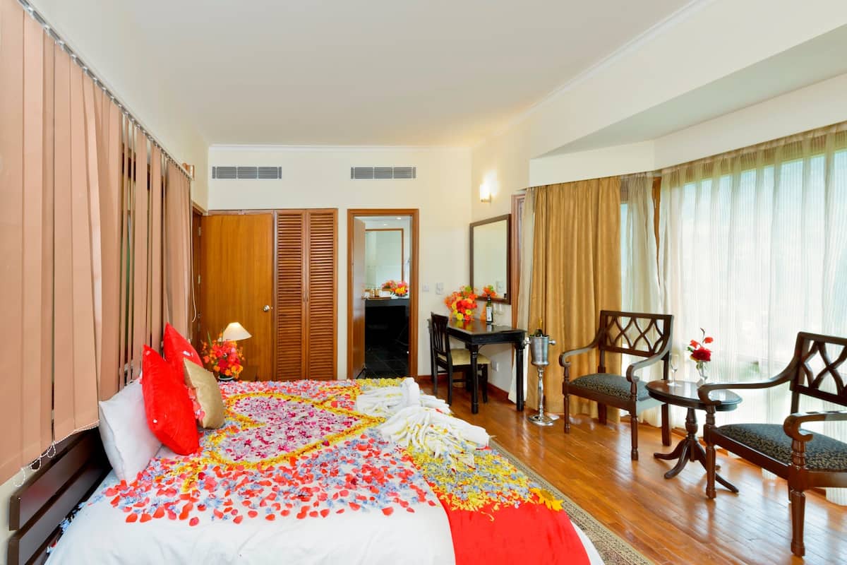 Una habitación de hotel con cama, escritorio, dos sillas, espejo y ventana con cortinas.