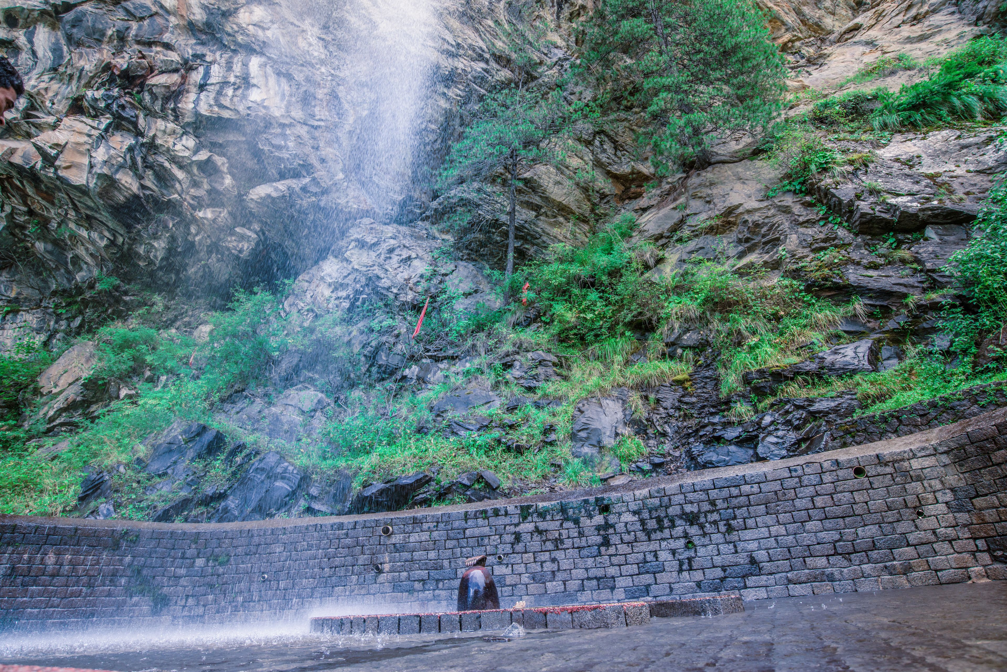 A stone retaining wall with a waterfall in the background.
