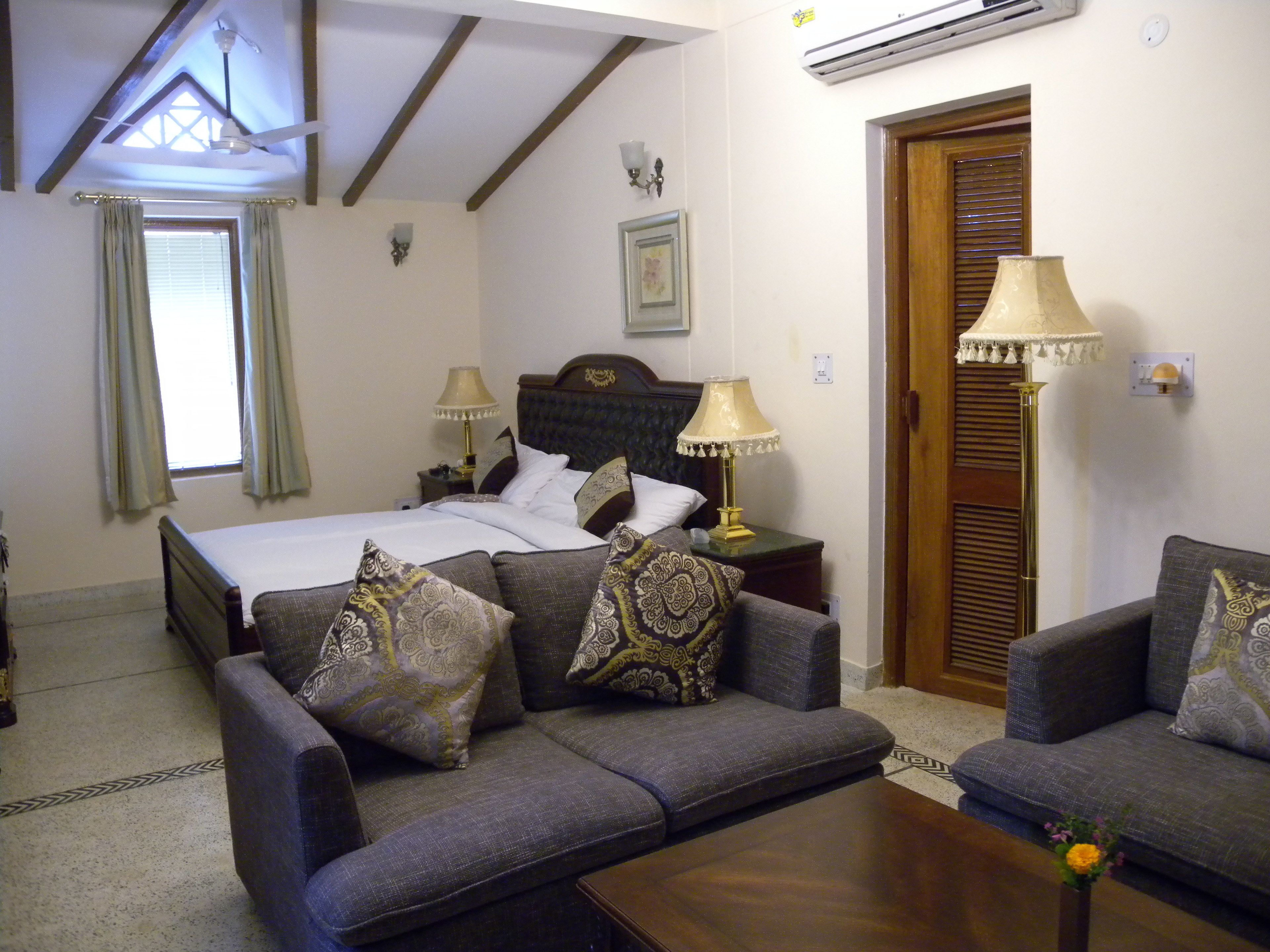 Una camera d'albergo con un letto, due divani, un tavolino da caffè, una lampada e un quadro appeso al muro.
