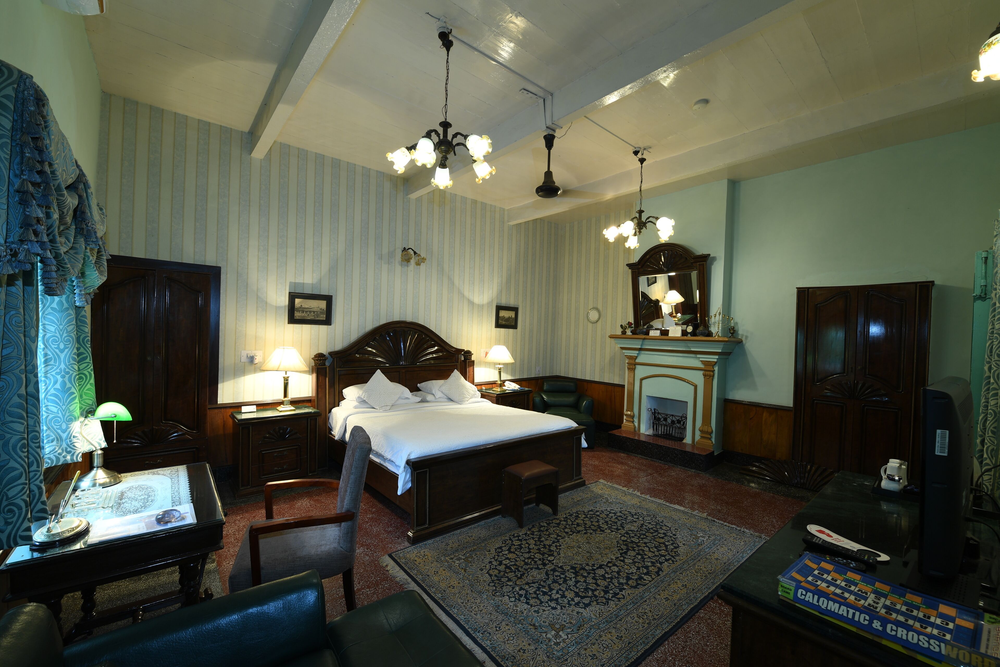 Quarto de hotel tradicional com uma cama grande, uma escrivaninha com abajur, lareira e televisão.