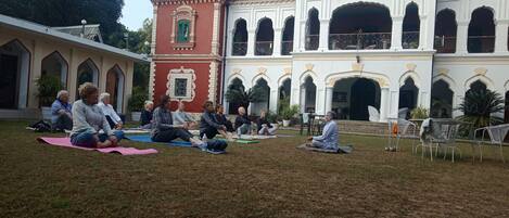 A courtyard with people sitting on mats, a building with arches, and a red tower.