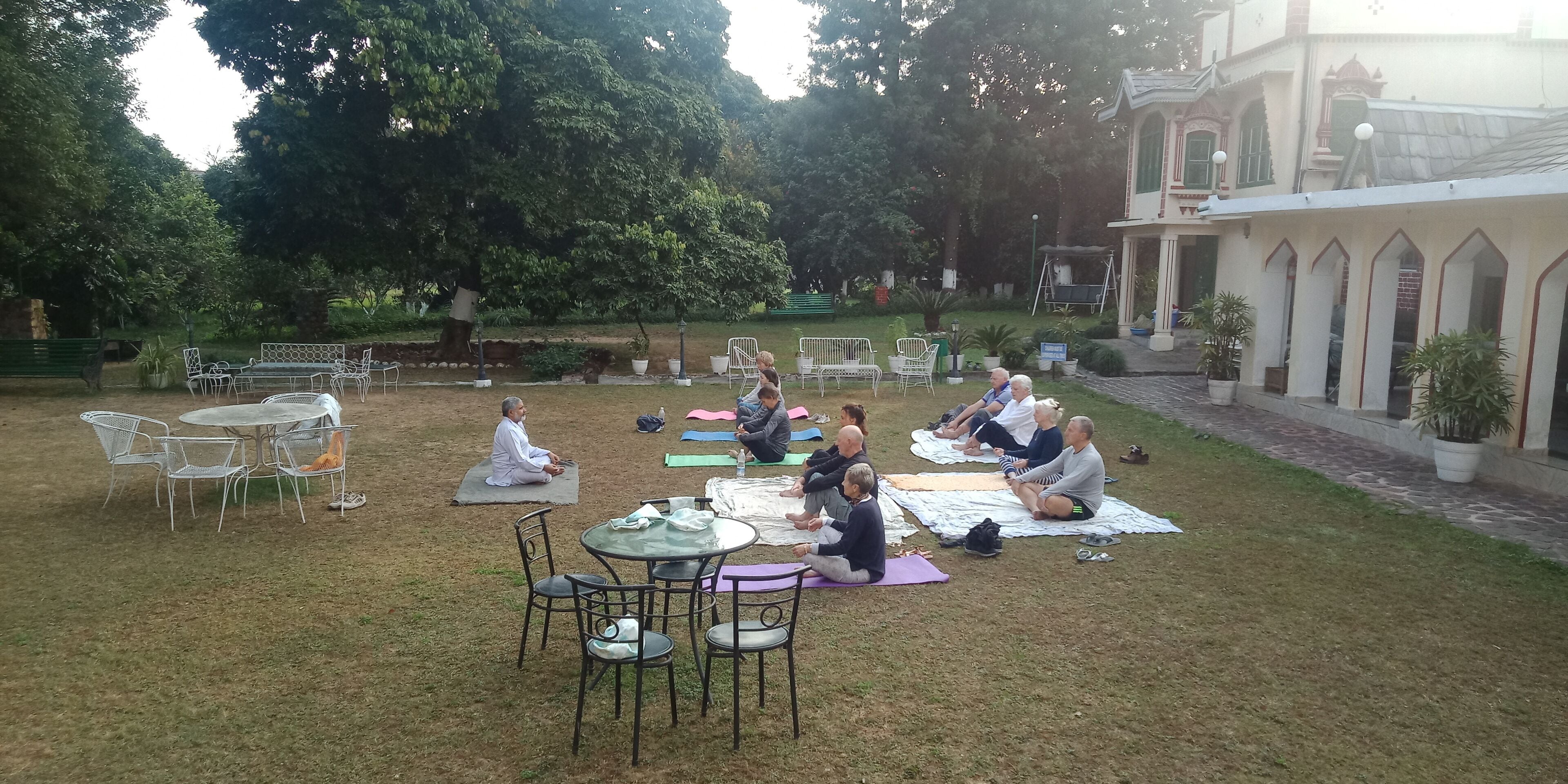 Un cours de yoga en plein air, dans un jardin agrémenté d’un kiosque, de tables et de chaises.