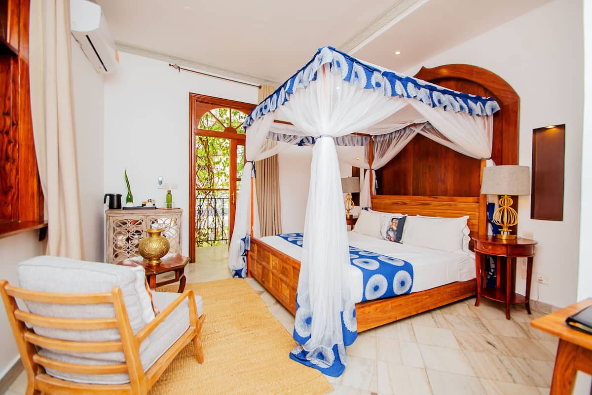 Un dormitorio con cama con dosel, cabecera de madera, mesita de noche con lámpara y un pequeño mueble de madera.