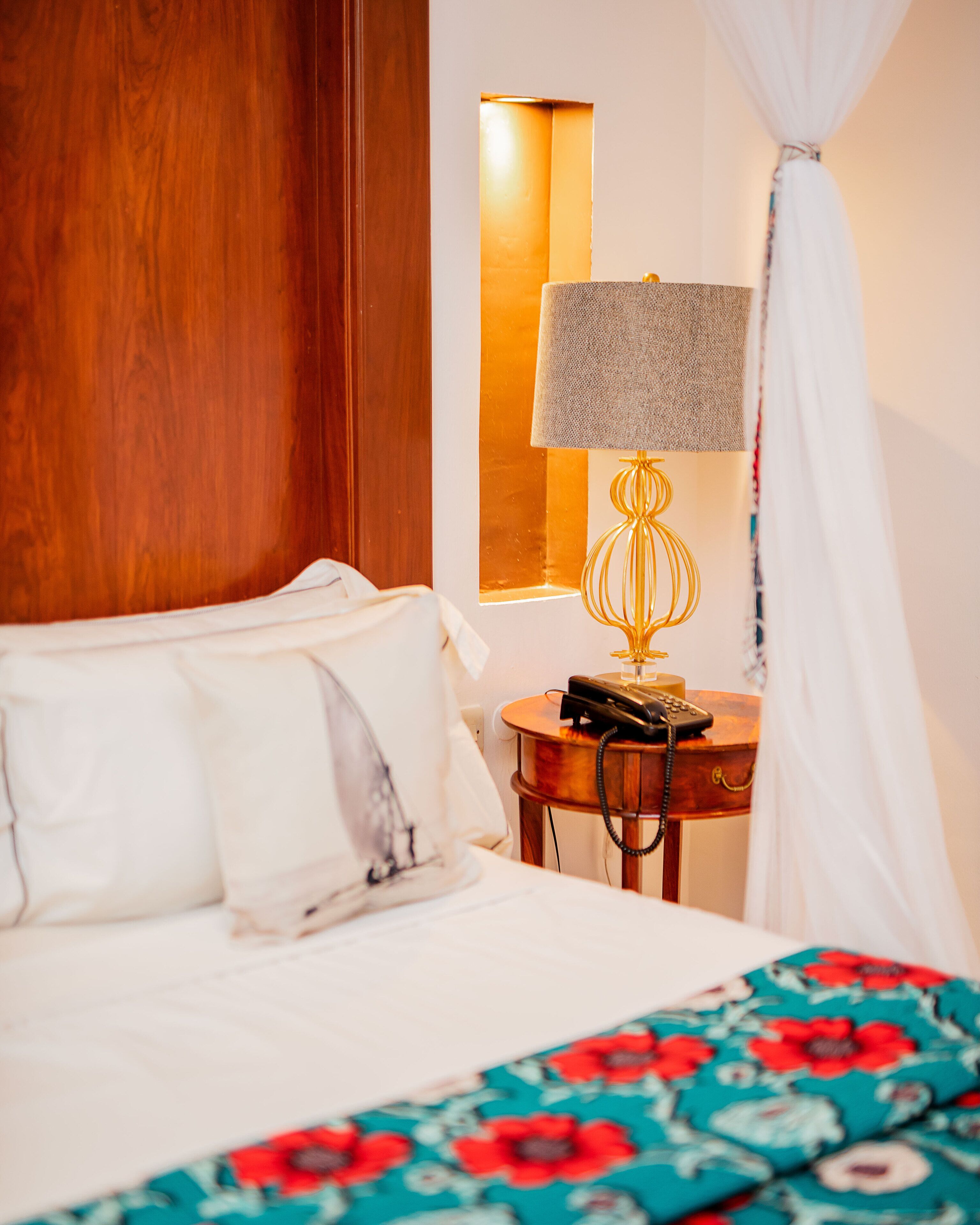 A neatly made bed with white linens, a bedside table with a lamp, and a telephone.