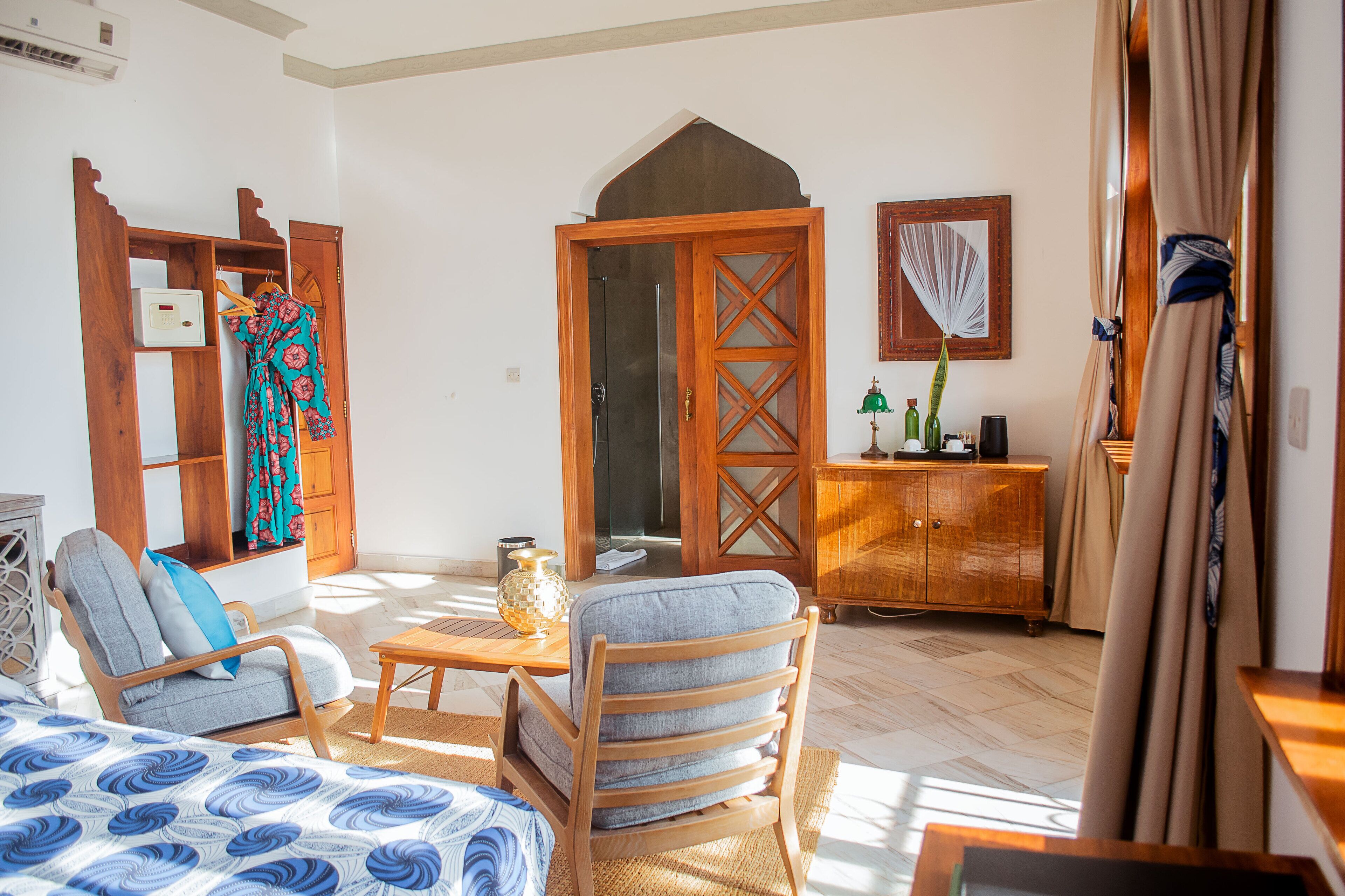 A room with a bed, a chair, a wooden cabinet, and a door leading to another room.