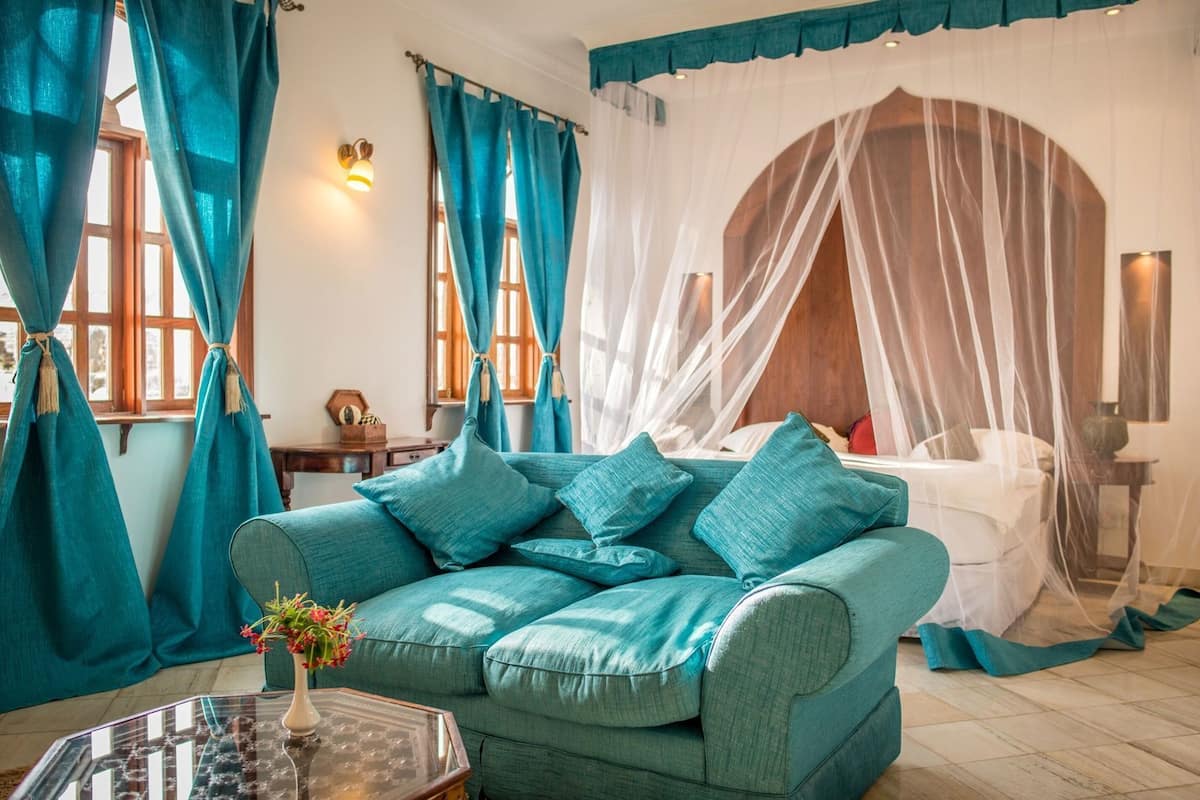 A room with a teal sofa, a bed with a canopy, and a small table with a vase.