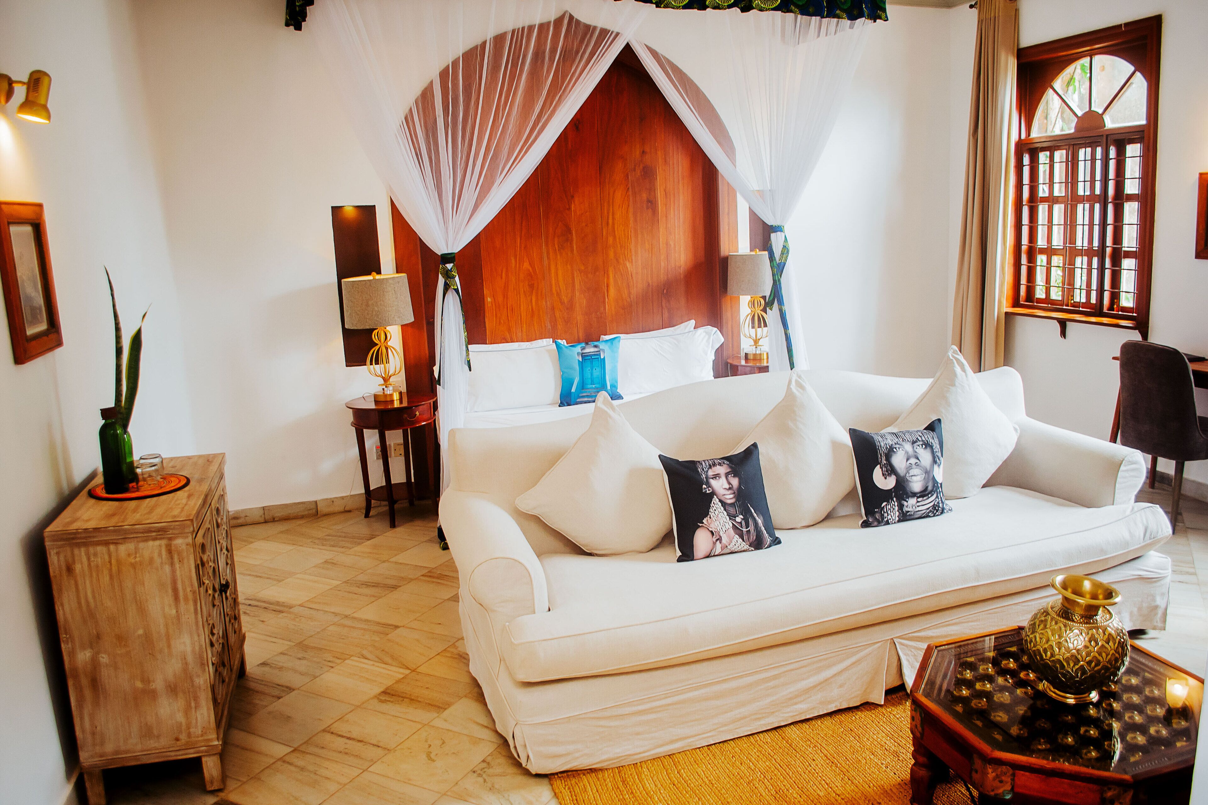 A white sofa with a canopy, a wooden cabinet, and a decorative table with a vase.