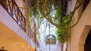 A narrow courtyard with a wooden balcony and a pathway lined with plants.