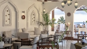 A spacious lounge area with comfortable seating, a large plant, and a view of the ocean.