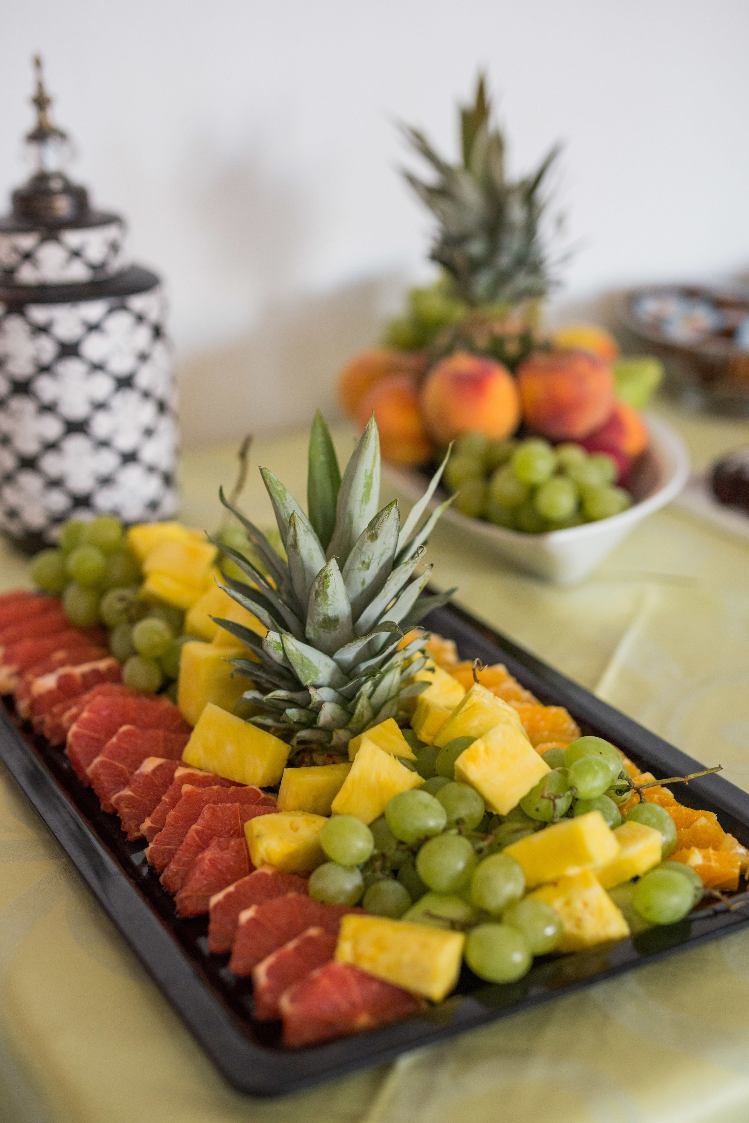 A fruit platter with pineapple, grapes, and mangoes on a tray.
