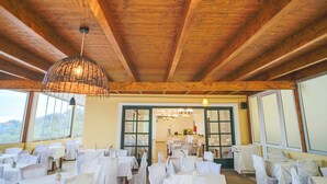 Un restaurante con vigas de madera, mesas blancas y un ventanal grande.