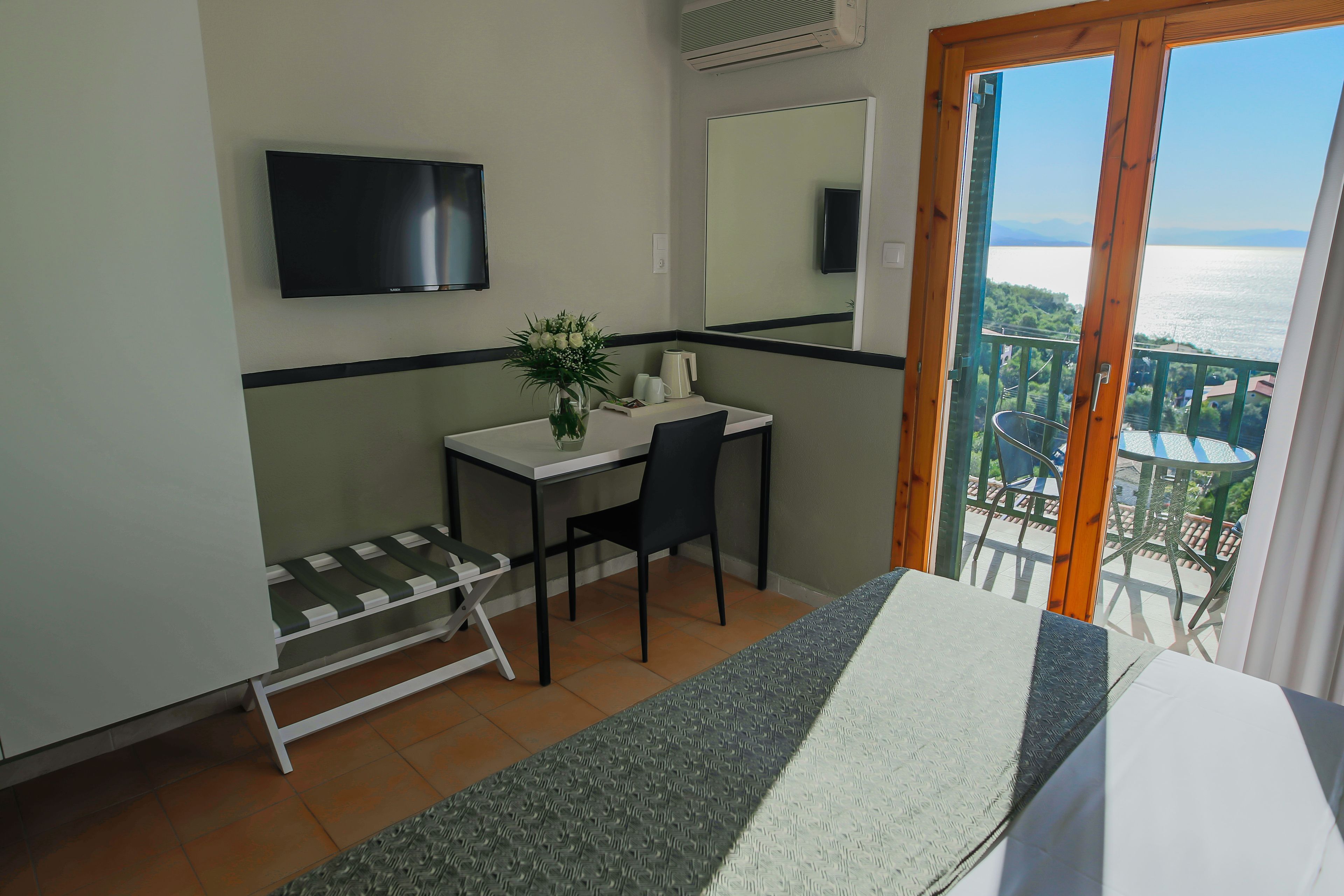 Quarto com cama, escrivaninha com cadeira, televisão, espelho e vista para o mar.