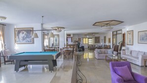 Amplia sala de estar con mesa de billar, sofás y comedor.