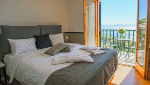 Habitación de hotel con cama, almohadas, una colcha impecable, una mesita con sillas y un balcón con vistas.