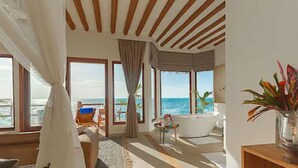 Una habitación amplia con un ventanal grande que ofrece vistas al mar, una bañera blanca y un techo de madera.