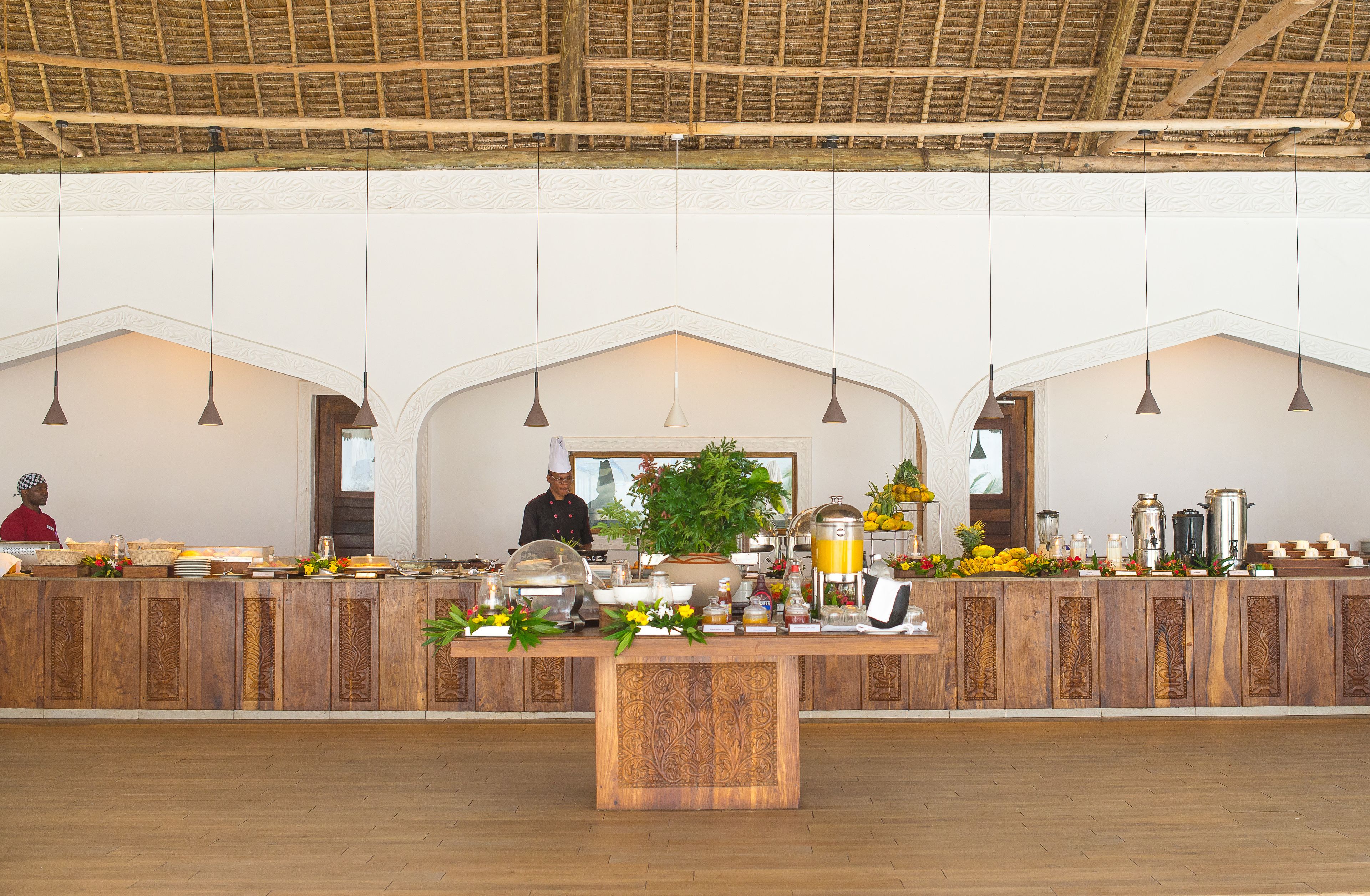 A buffet setup with a wooden counter, hanging pendant lights, and a central decorative plant.