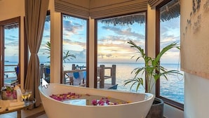 Una bañera grande llena de agua y flores, ubicada cerca de amplios ventanales con vistas al mar.