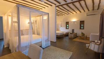 A room with a four-poster bed, a sitting area with a sofa and armchairs, a small table, and a wooden floor.