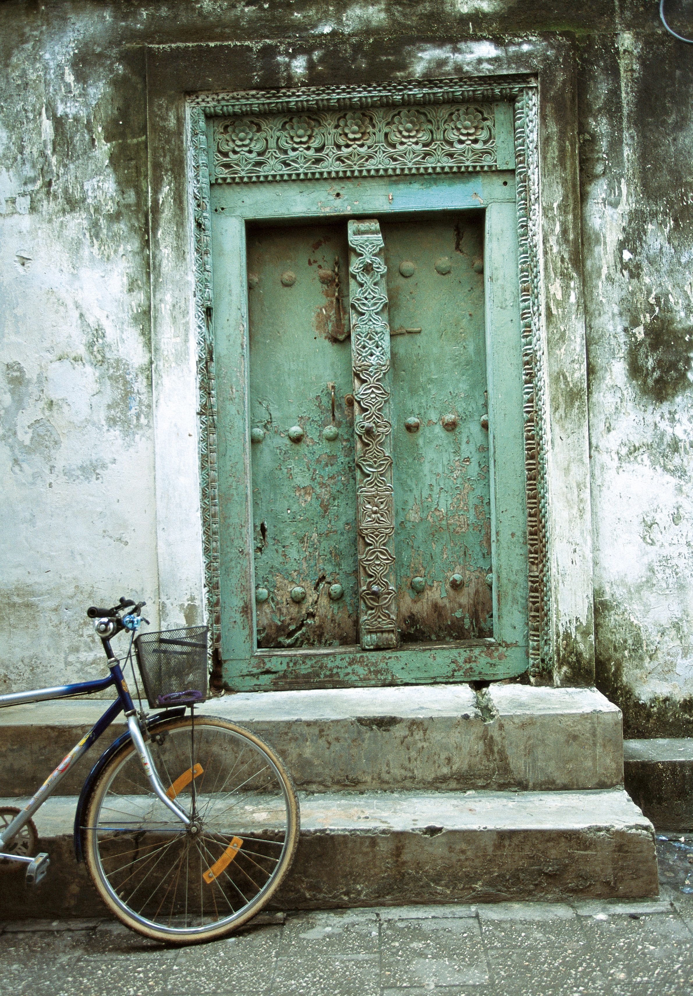 A bicycle parked in front of a weathered, ornate door with a metal handle and decorative elements.