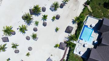 Vista aérea de un resort con piscina, palmeras y zona de playa.