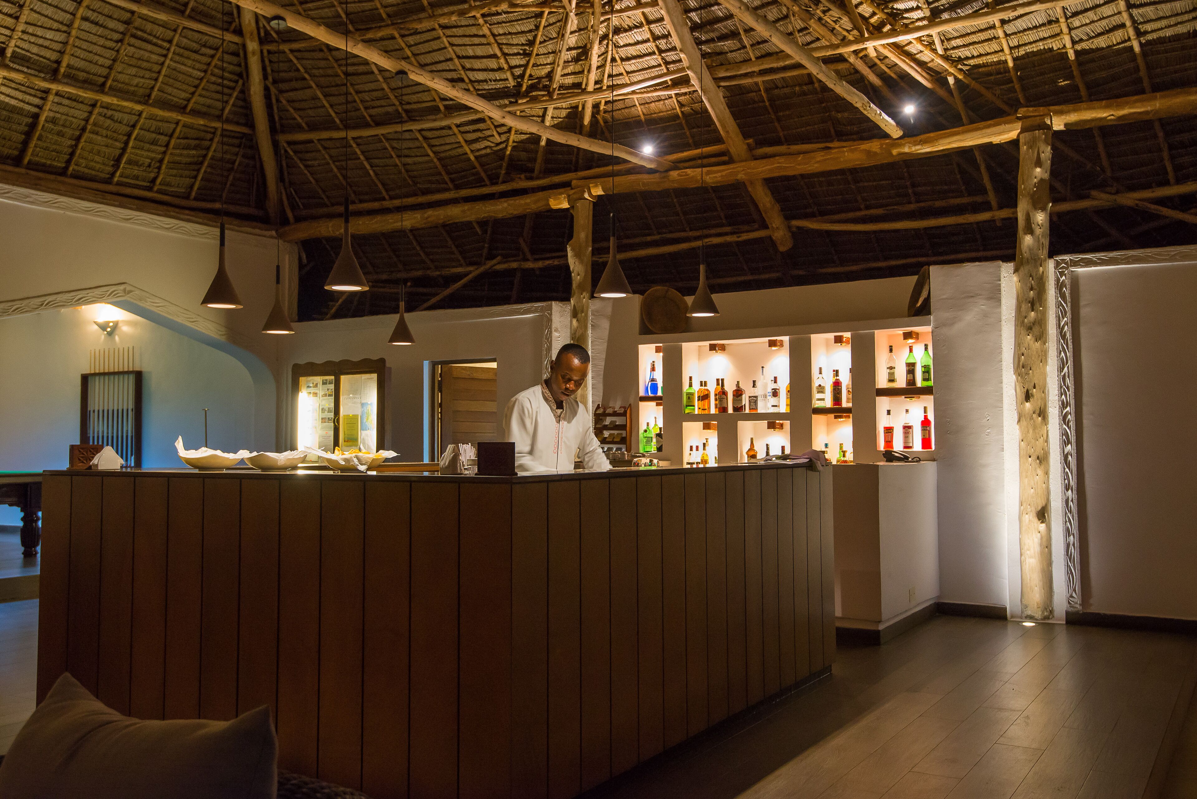 A bar area with wooden paneling, hanging pendant lights, and shelves with bottles.