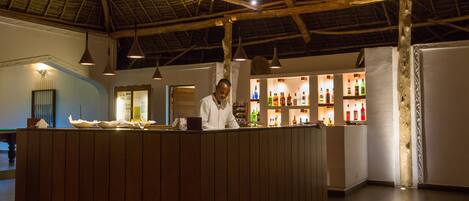 A bar area with wooden paneling, hanging pendant lights, and shelves with bottles.
