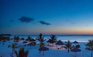 A beach with thatched umbrellas and palm trees.