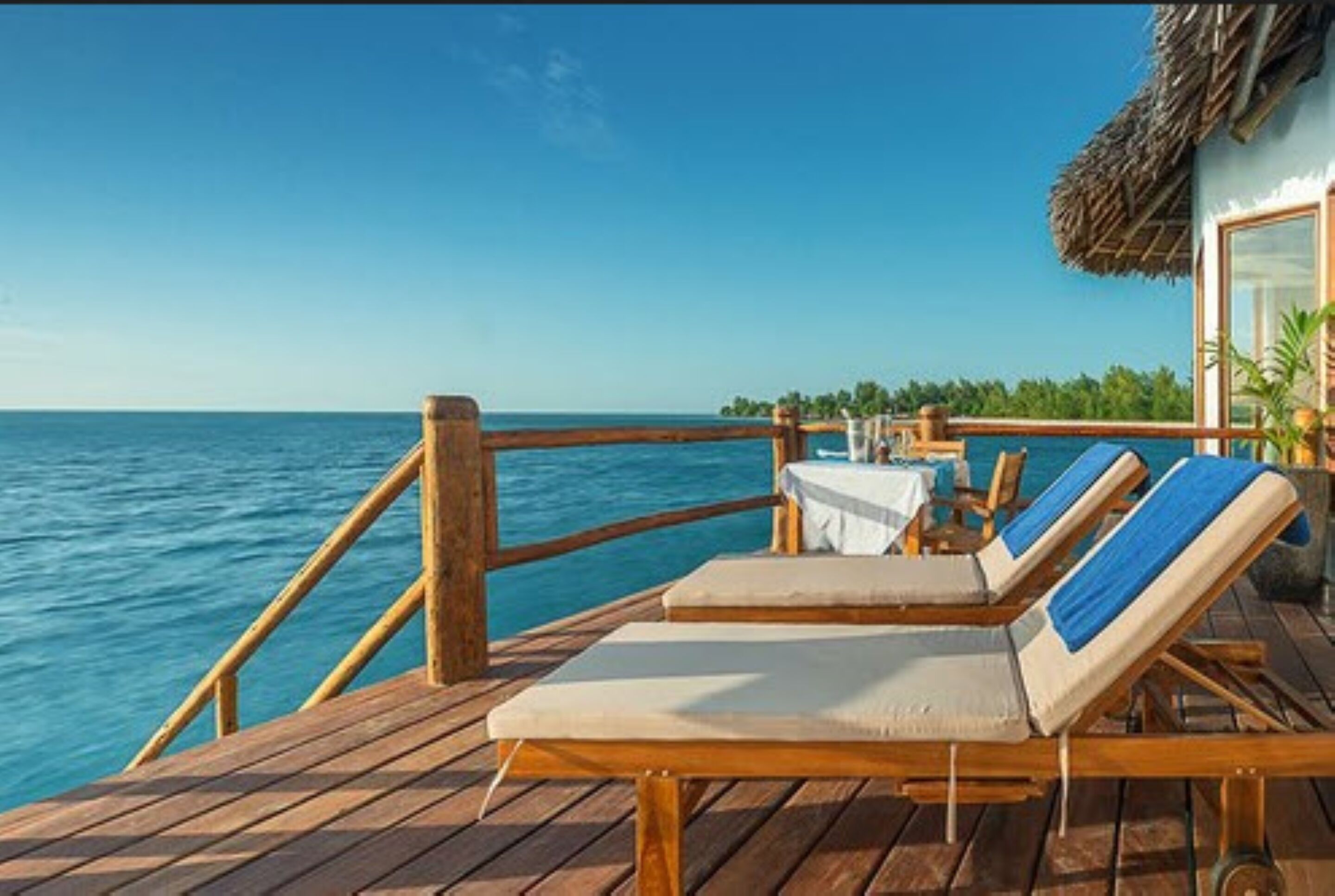 A wooden deck with two lounge chairs and a table, overlooking a calm sea.