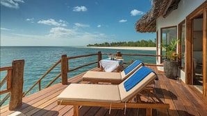 Terraza de madera con sillones de descanso y una mesa con vista a la playa y al océano.