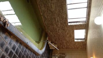 A bathroom with a green tiled floor, a bathtub, and a shower area. There are windows allowing natural light to enter.
