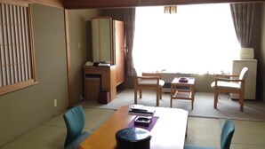 Una habitación con una mesa de madera, dos sillas, un escritorio pequeño con un espejo y una ventana con cortinas.