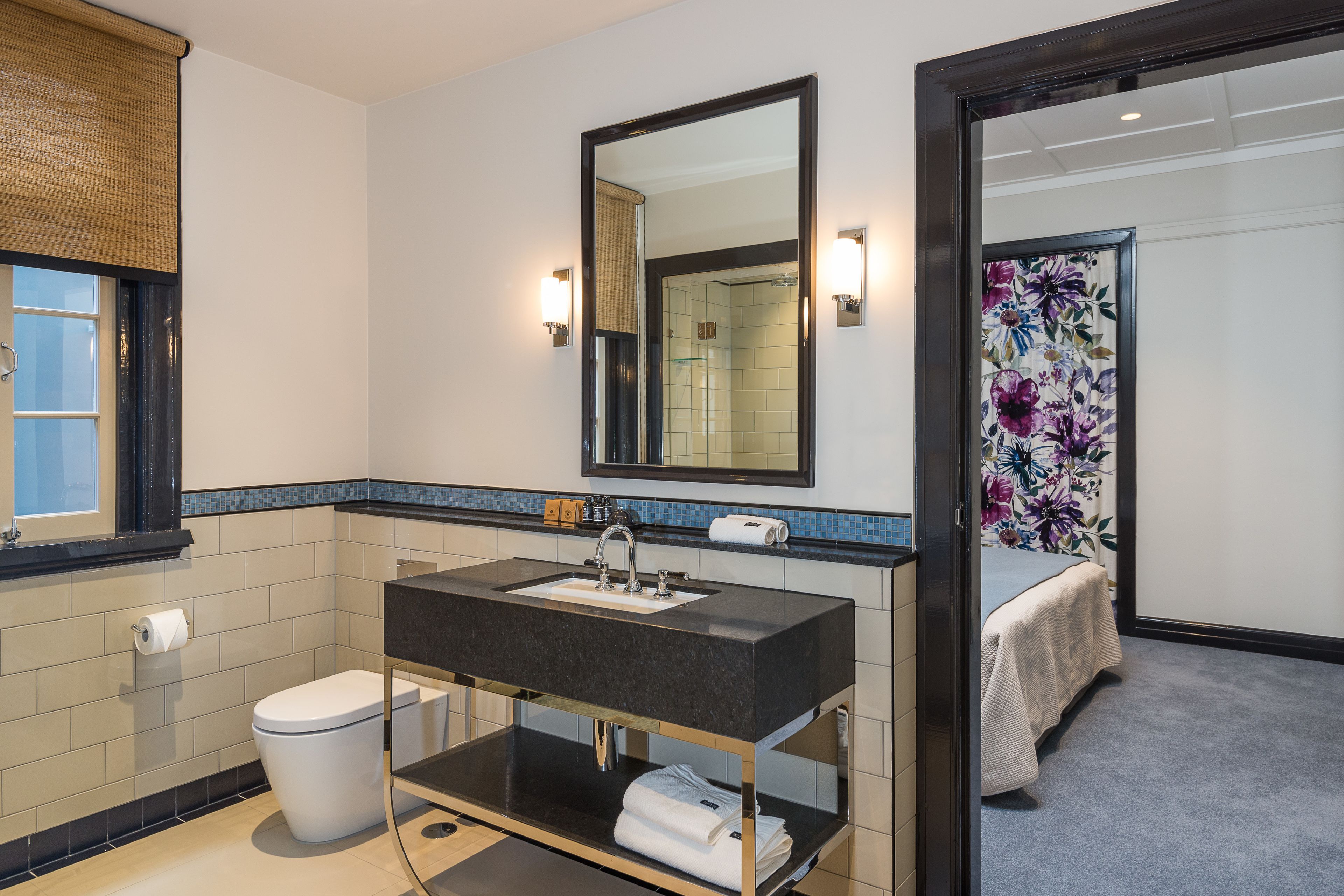 Un baño moderno con un lavabo negro, inodoro blanco y un espejo grande.