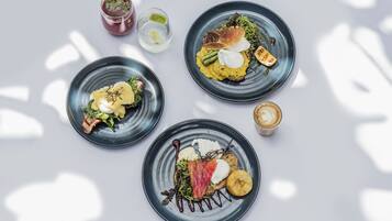 Three plates of food with various items including greens, meats, and sauces, and two drinks on a white surface.