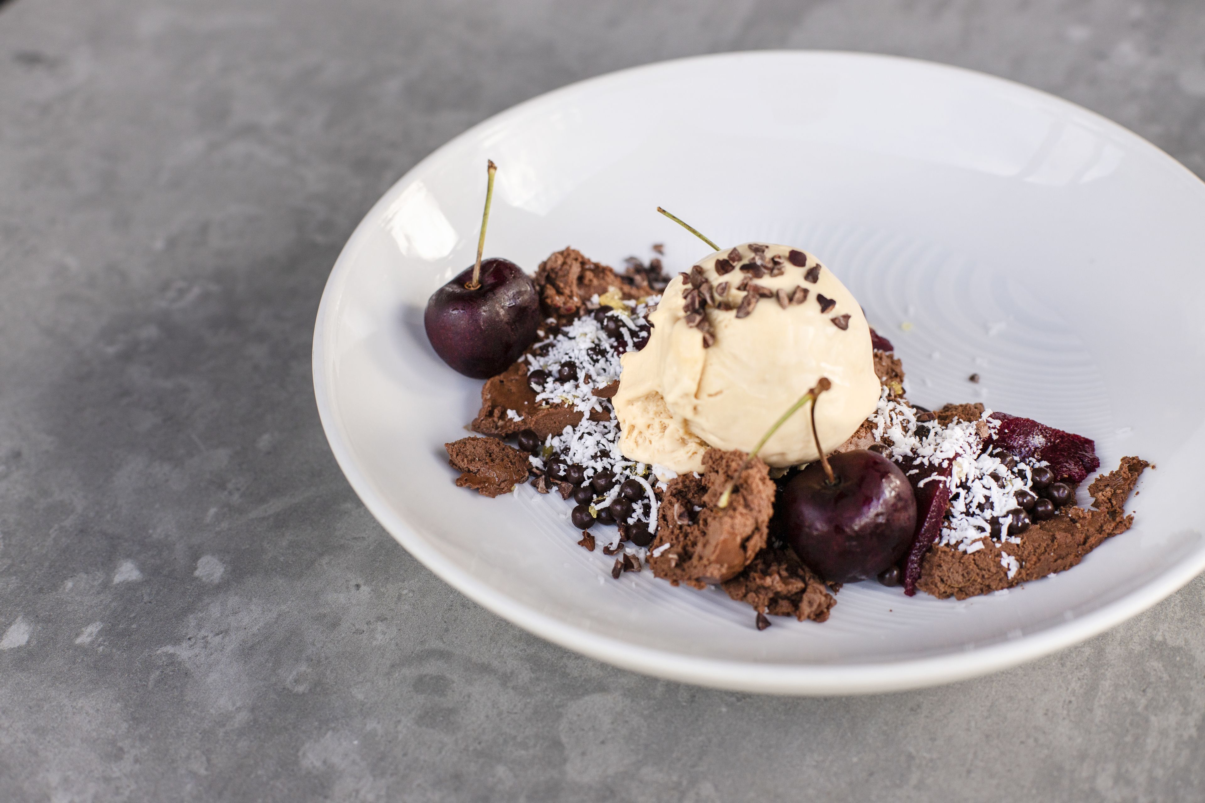 A dessert plate with ice cream, cherries, chocolate pieces, and shredded coconut.