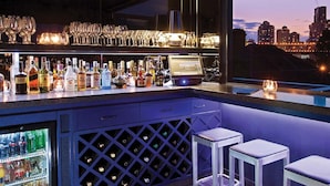 Un bar con vistas a un horizonte urbano, botellas de licor, vasos y un enfriador de vino.