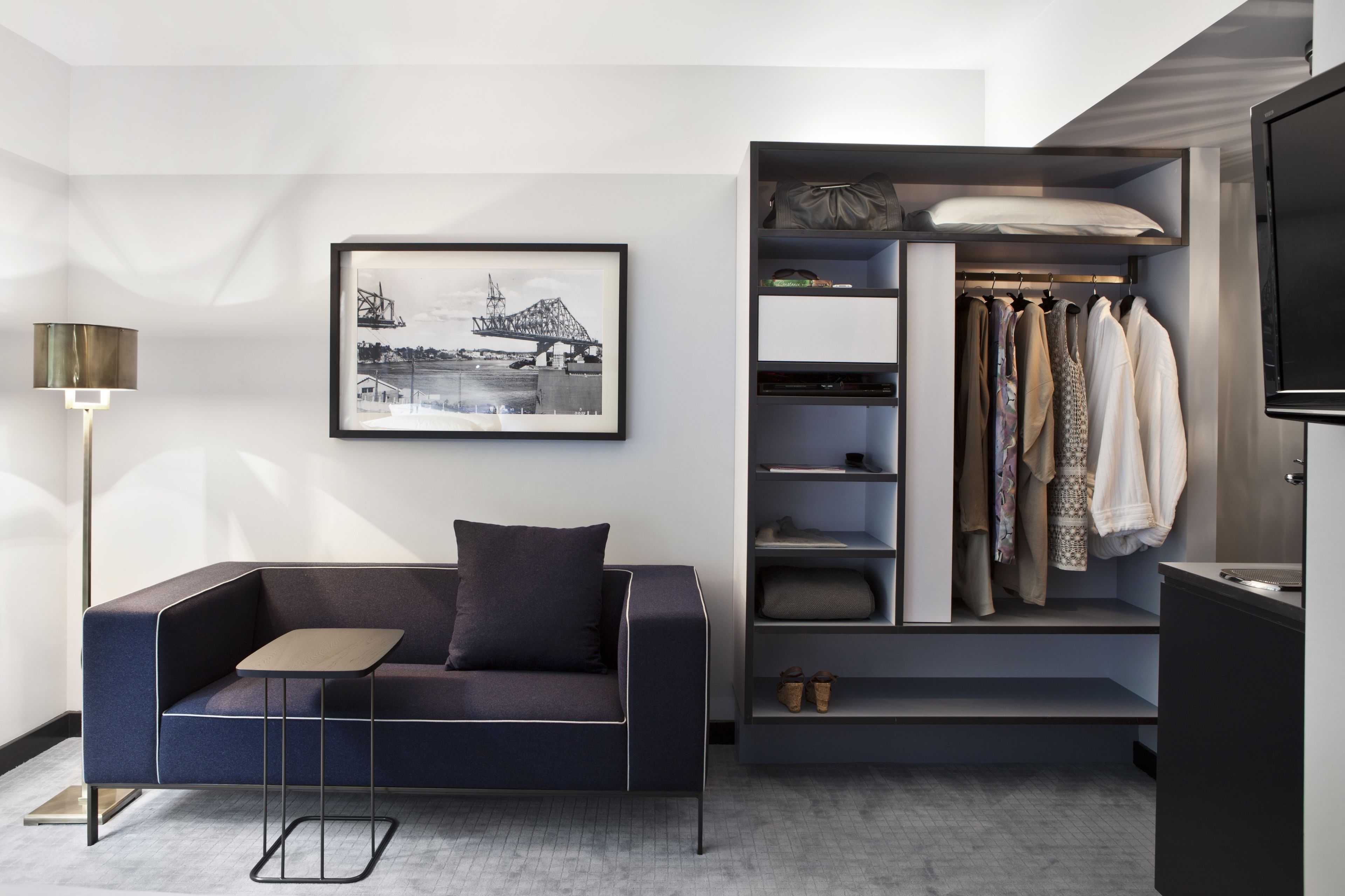 A modern living room with a sofa, a small table, a framed picture, a closet with hanging clothes, and a TV.