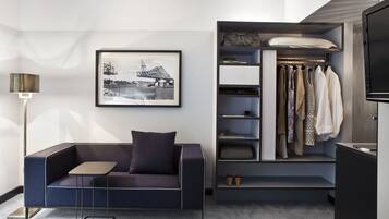 A modern living room with a sofa, a small table, a framed picture, a closet with hanging clothes, and a TV.