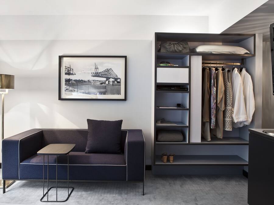 A modern living room with a sofa, a small table, a framed picture, a closet with hanging clothes, and a TV.